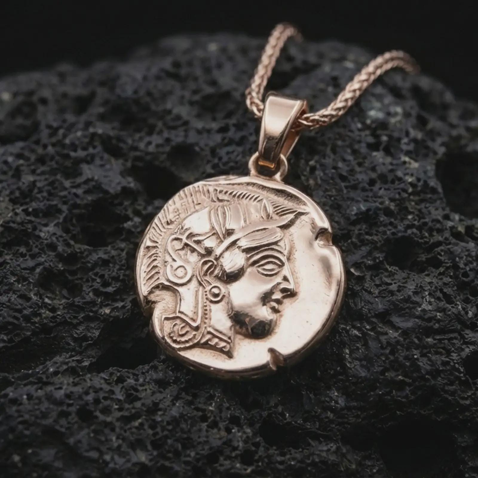 Rose gold plated Athena owl coin pendant necklace presented on textured volcanic stone, showcasing the owl emblem, engraved ancient symbols, and weathered coin-inspired surface in a macro studio shot.