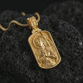 Load image into Gallery viewer, Gold plated Joan of Arc dog tag pendant necklace photographed on porous black volcanic stone, emphasizing the sacred warrior figure and elegant Catholic medal composition in a luxury jewelry shot.
