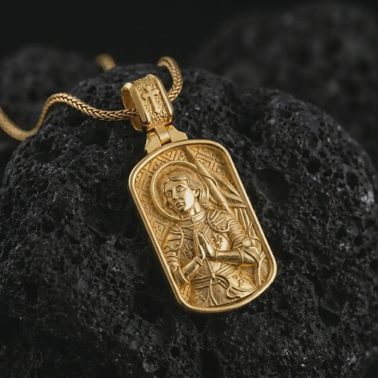 Gold plated Joan of Arc dog tag pendant necklace photographed on porous black volcanic stone, emphasizing the sacred warrior figure and elegant Catholic medal composition in a luxury jewelry shot.