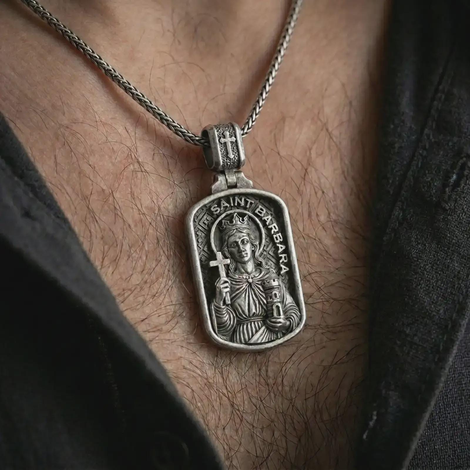 Oxidized Saint Barbara pendant necklace worn on the chest, close-up lifestyle jewelry photo showing the religious medallion on a spiga chain with dark clothing.