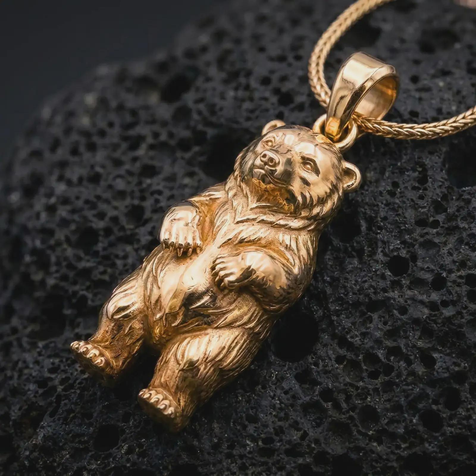 Gold plated baby bear pendant necklace on textured volcanic rock, premium close-up studio composition emphasizing the playful bear cub shape, soft expression, and woodland animal charm.