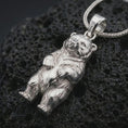 Load image into Gallery viewer, Polished silver baby bear pendant necklace on textured volcanic rock, centered macro jewelry photo with detailed bear cub sculpting and bright silver highlights.
