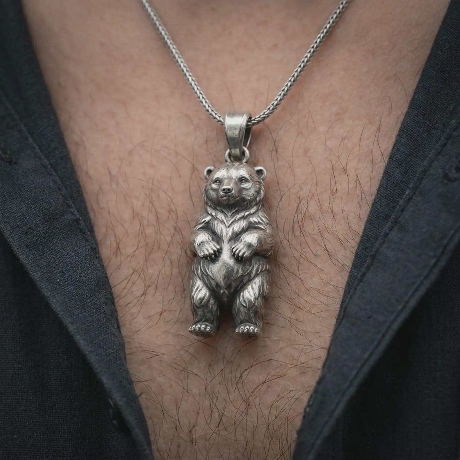 Oxidized baby bear pendant necklace worn on the chest, close-up lifestyle jewelry photo showing the bear cub charm on a spiga chain with dark clothing.