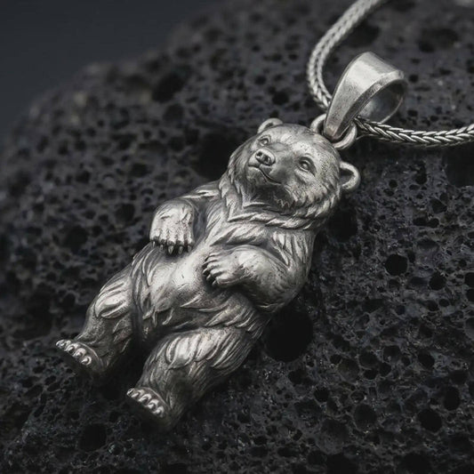 Oxidized baby bear pendant necklace on textured volcanic rock, close-up studio shot highlighting the cute bear cub charm, rounded paws, detailed fur, and antique silver contrast.