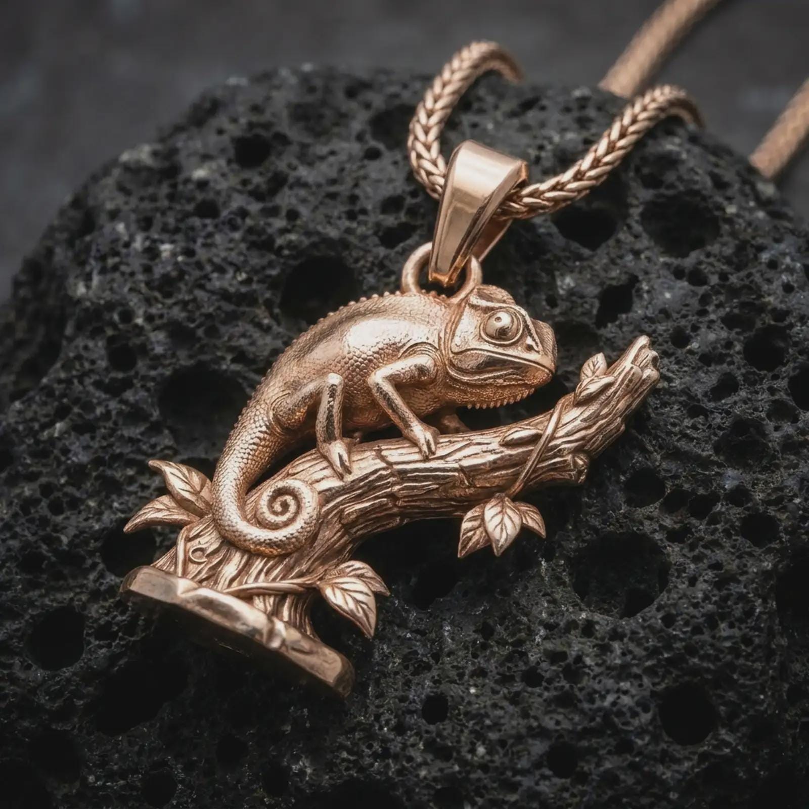 Rose gold plated chameleon pendant necklace on textured volcanic rock, detailed macro product shot with soft warm reflections and unique reptile jewelry styling.