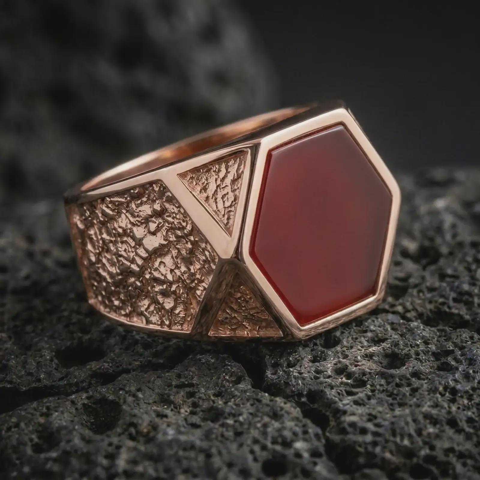 A red onyx signet ring in a rose gold plated finish resting on porous volcanic rock in a premium macro studio shot.