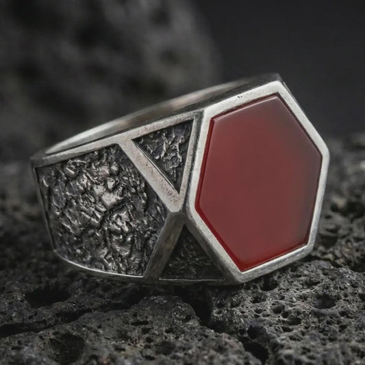 A red onyx signet ring in an oxidized finish resting on porous volcanic rock in a premium macro studio shot.