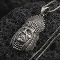 Load image into Gallery viewer, Oxidized feather headdress chief pendant necklace on textured volcanic rock, close-up studio shot highlighting the sculpted face, feather details, beaded necklace, and antique silver contrast.
