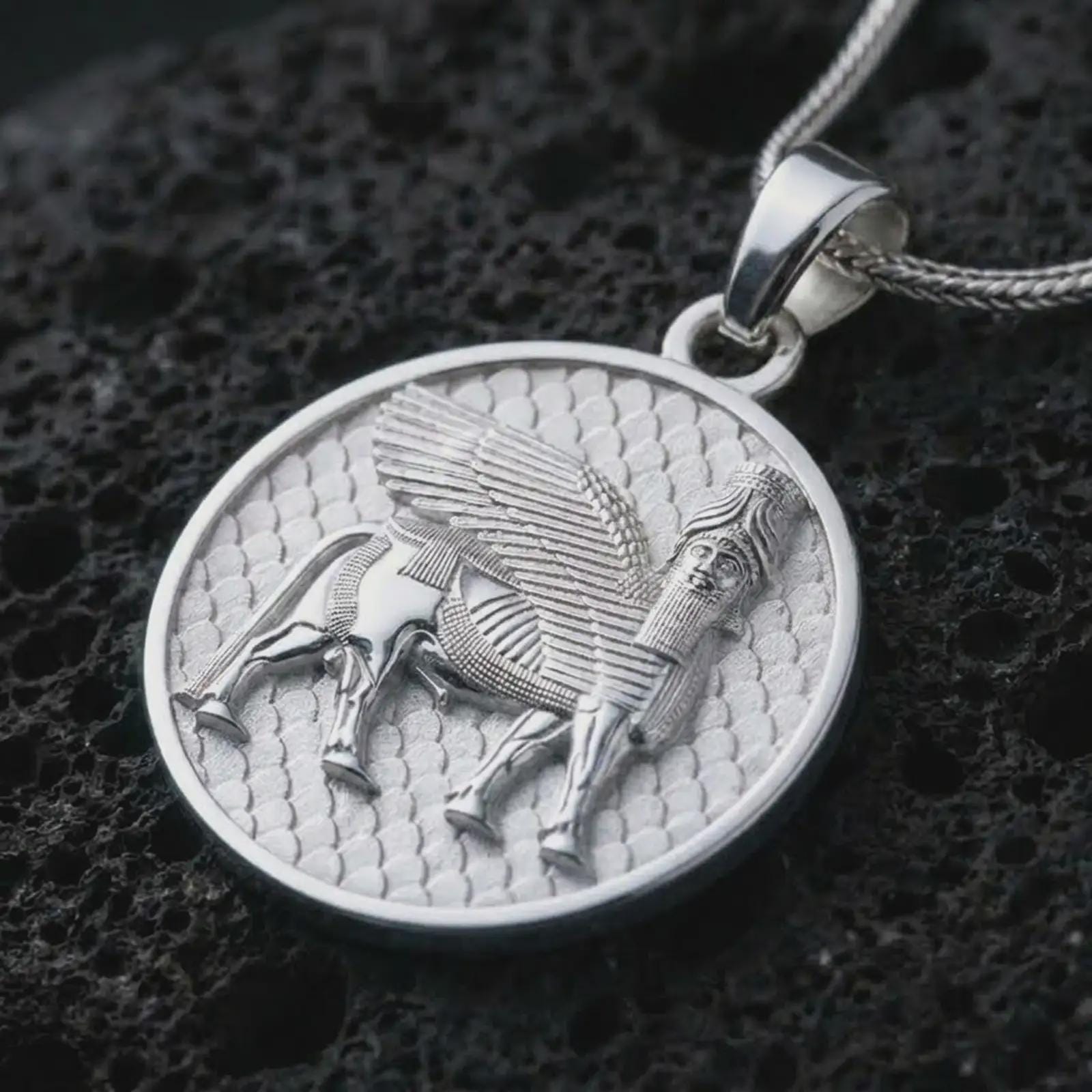 Polished silver Assyrian Lamassu pendant necklace on textured volcanic rock, centered macro jewelry photo with detailed Mesopotamian guardian spirit relief and bright silver highlights.
