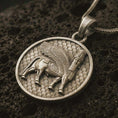 Load image into Gallery viewer, Bronze Assyrian Lamassu pendant necklace on textured volcanic rock, close-up studio shot highlighting the winged guardian bull, ancient relief details, and antique silver contrast.
