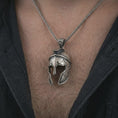 Load image into Gallery viewer, Oxidized Spartan helmet pendant necklace worn on the chest, close-up lifestyle jewelry photo showing the warrior helmet charm on a spiga chain with dark clothing.
