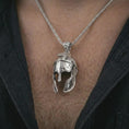 Load image into Gallery viewer, Polished silver Spartan helmet pendant necklace worn on the chest, masculine lifestyle shot highlighting the cracked helmet relief, sculpted face guard, and bright silver finish.
