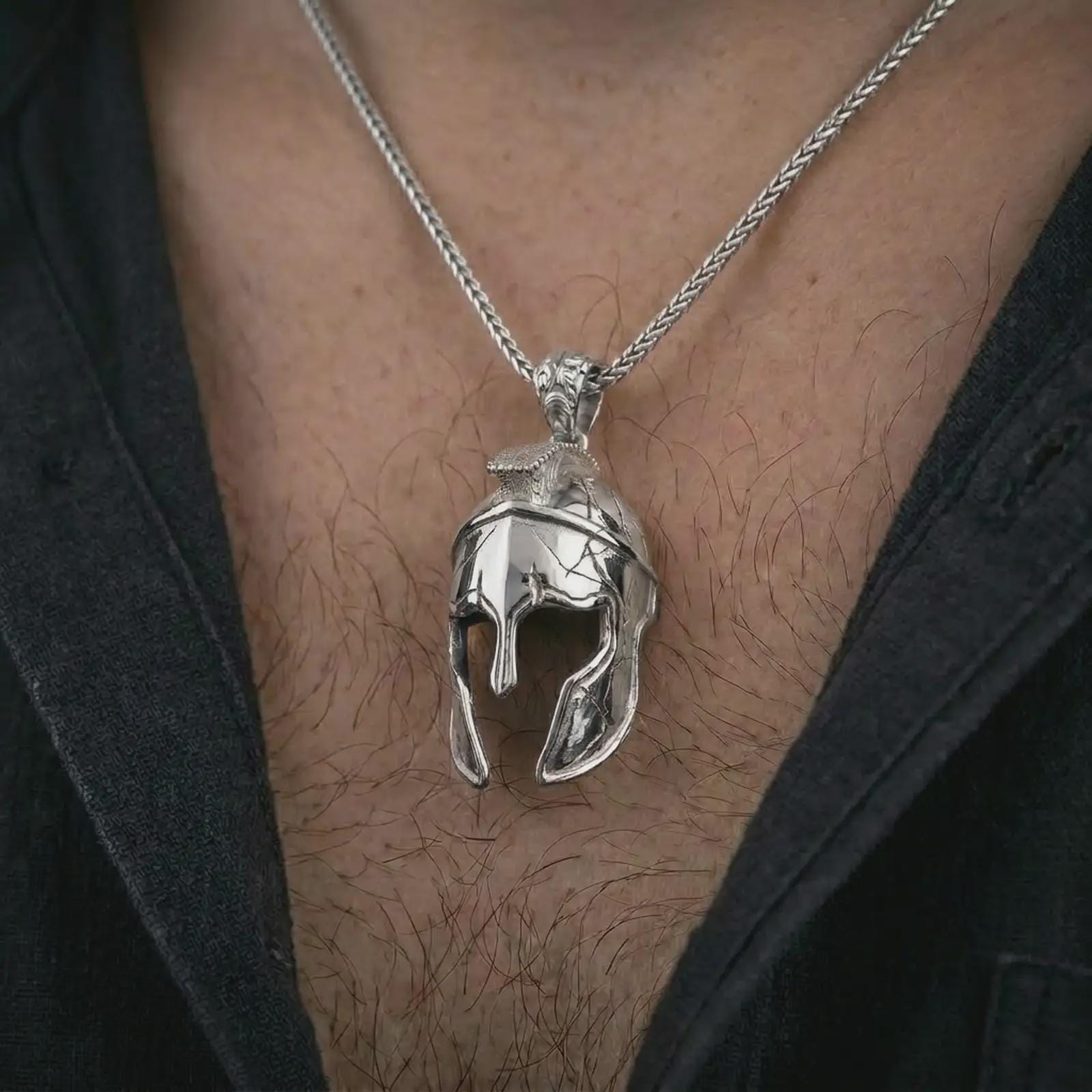 Polished silver Spartan helmet pendant necklace worn on the chest, masculine lifestyle shot highlighting the cracked helmet relief, sculpted face guard, and bright silver finish.