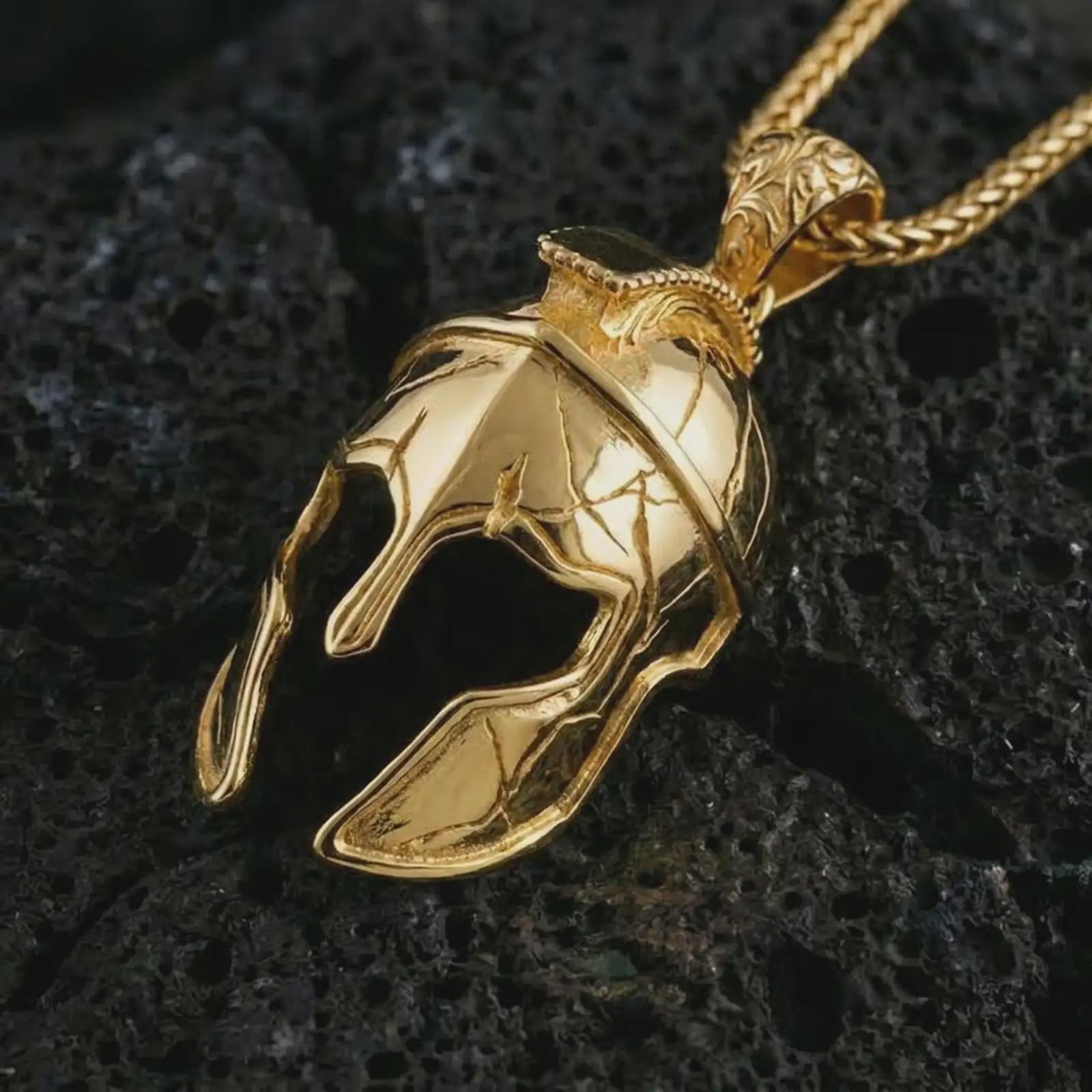 Gold plated Spartan helmet pendant necklace on textured volcanic rock, premium close-up studio composition emphasizing the battle helmet shape, cracked armor texture, and heroic warrior symbolism.