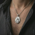 Load image into Gallery viewer, Polished silver Good Shepherd Jesus pendant necklace worn on the chest, masculine lifestyle shot highlighting the shepherd relief, lamb detail, and bright silver finish.
