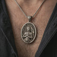 Load image into Gallery viewer, Oxidized Saint Joan of Arc pendant necklace worn on the chest, close-up lifestyle jewelry photo showing the religious medallion on a spiga chain with dark clothing.
