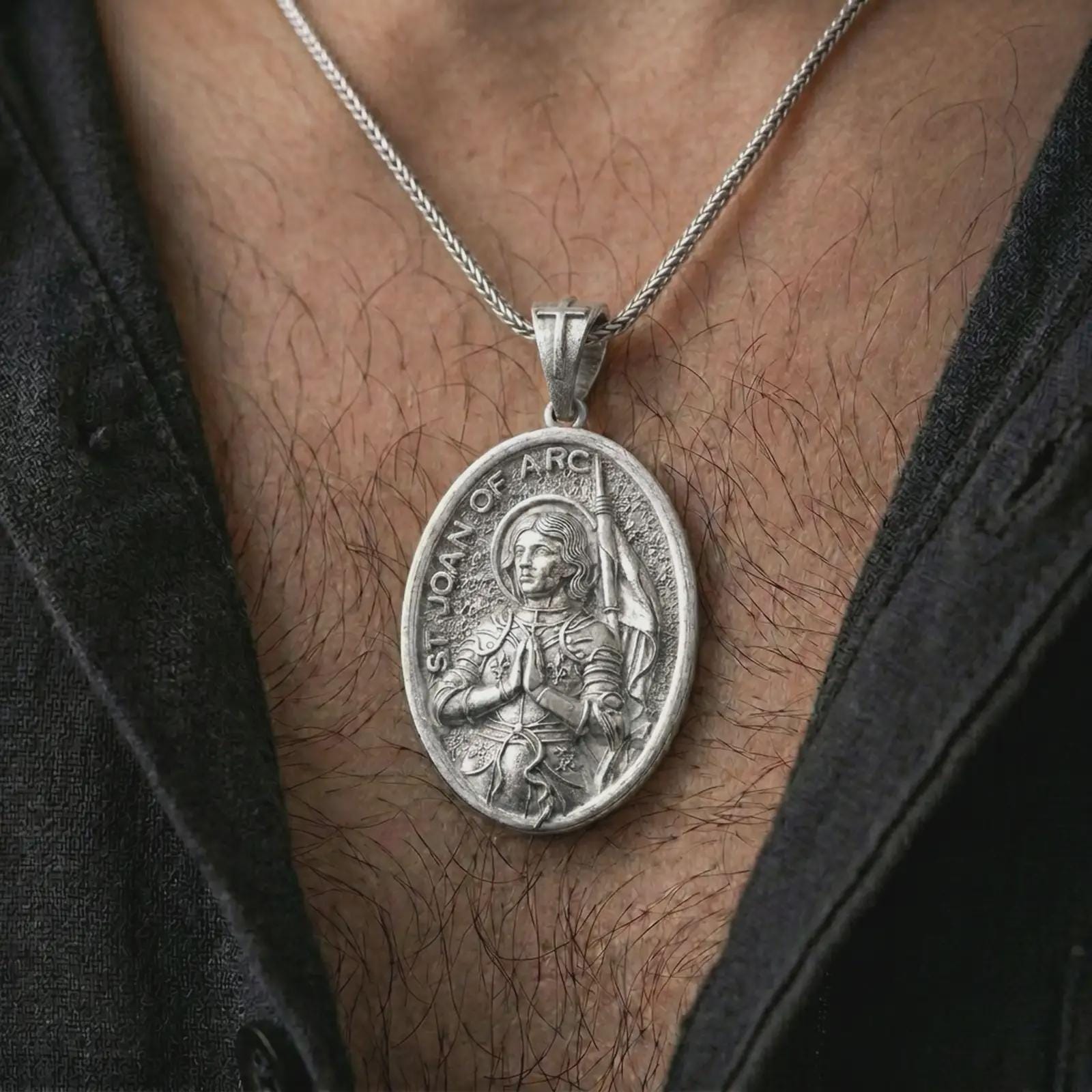 Polished silver Saint Joan of Arc pendant necklace worn on the chest, masculine lifestyle shot highlighting the armored saint relief, halo, and bright silver finish.