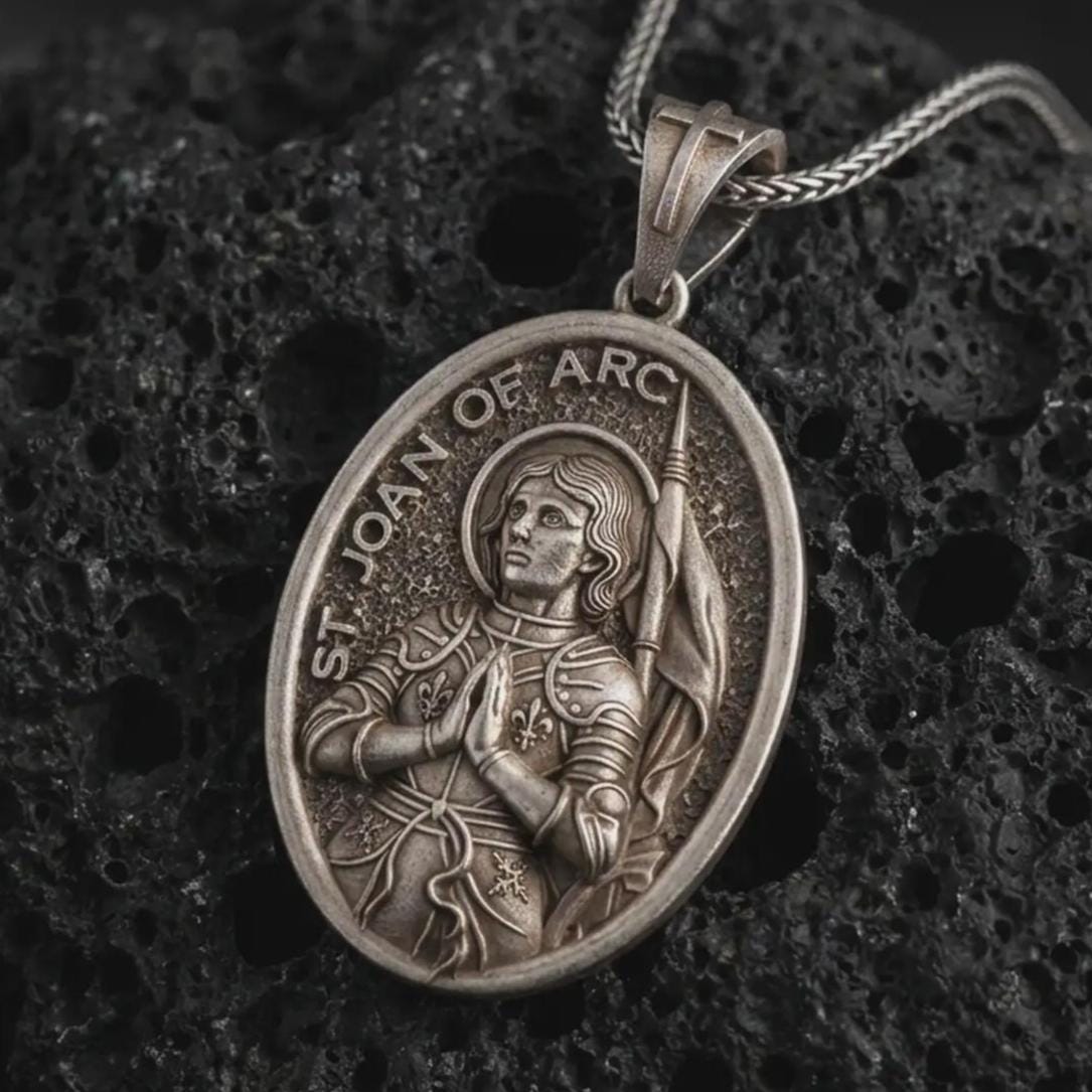 Oxidized Saint Joan of Arc pendant necklace on textured volcanic rock, close-up studio shot highlighting the armored saint relief, halo, banner, and antique silver contrast.