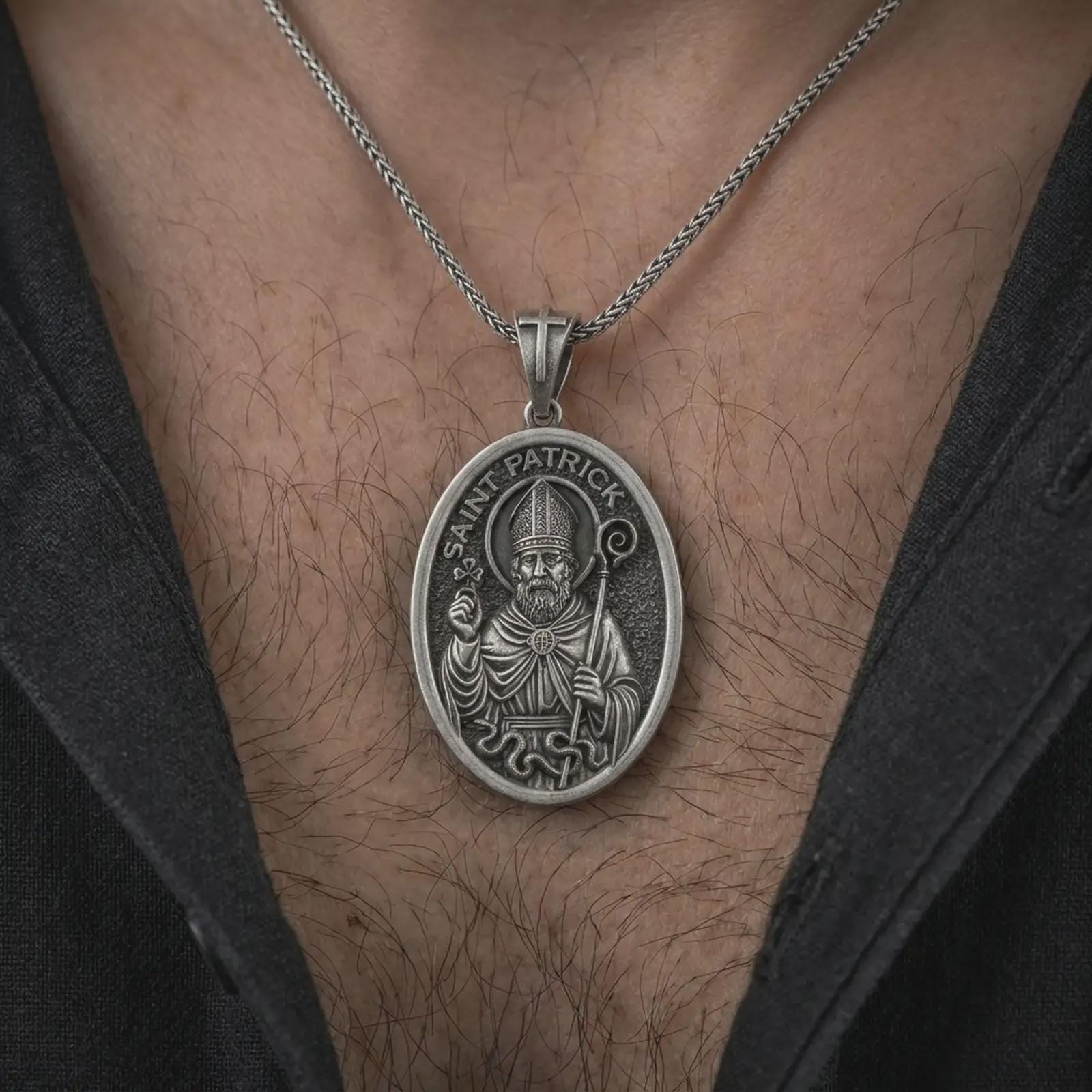 Oxidized Saint Patrick pendant necklace worn on the chest, close-up lifestyle jewelry photo showing the religious medallion on a spiga chain with dark clothing.