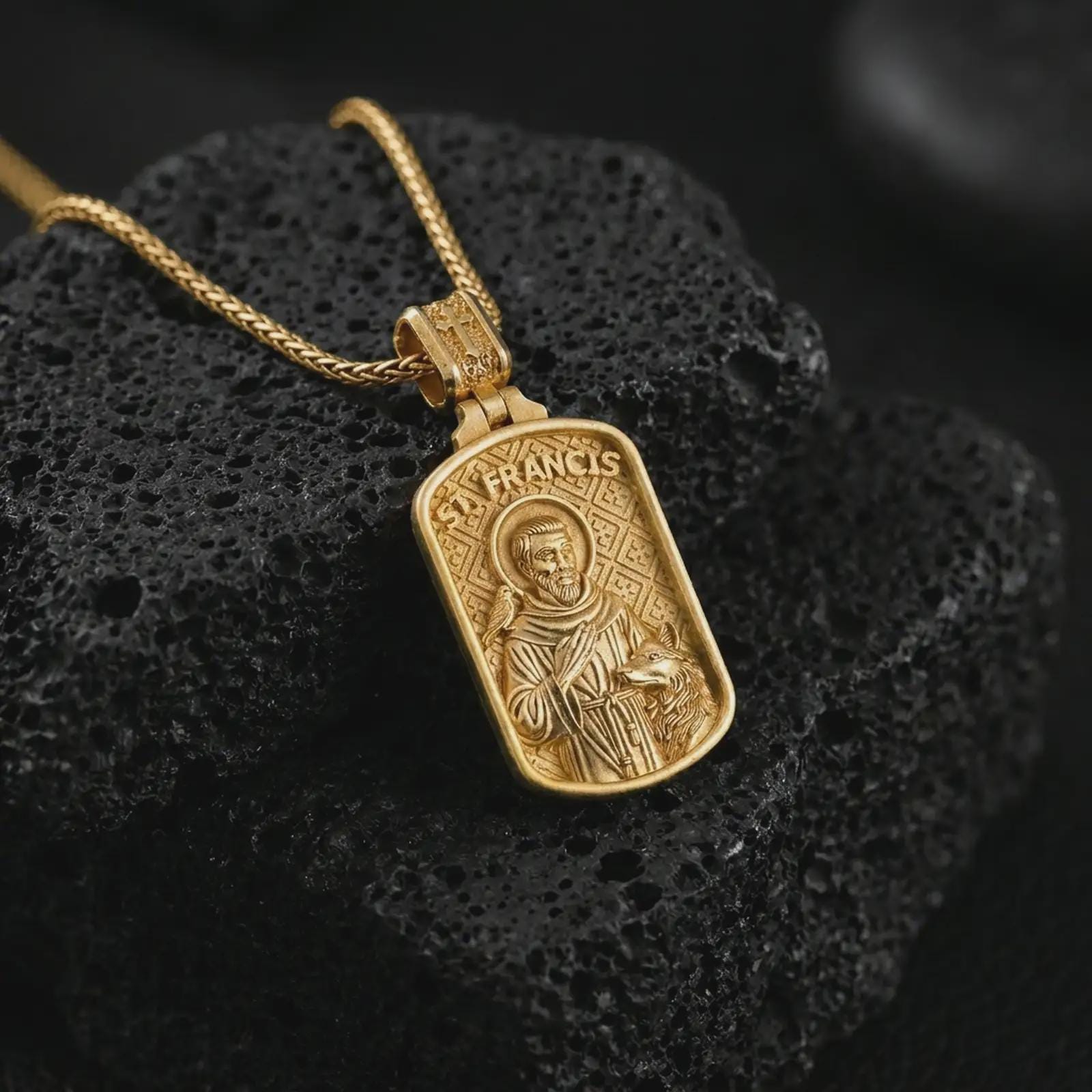 Gold plated Saint Francis pendant necklace on textured volcanic rock, premium close-up studio composition emphasizing the saint figure, bird, and wolf symbolism.