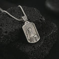 Load image into Gallery viewer, Polished silver Saint Francis pendant necklace on textured volcanic rock, centered macro jewelry photo with detailed religious engraving and bright silver highlights.
