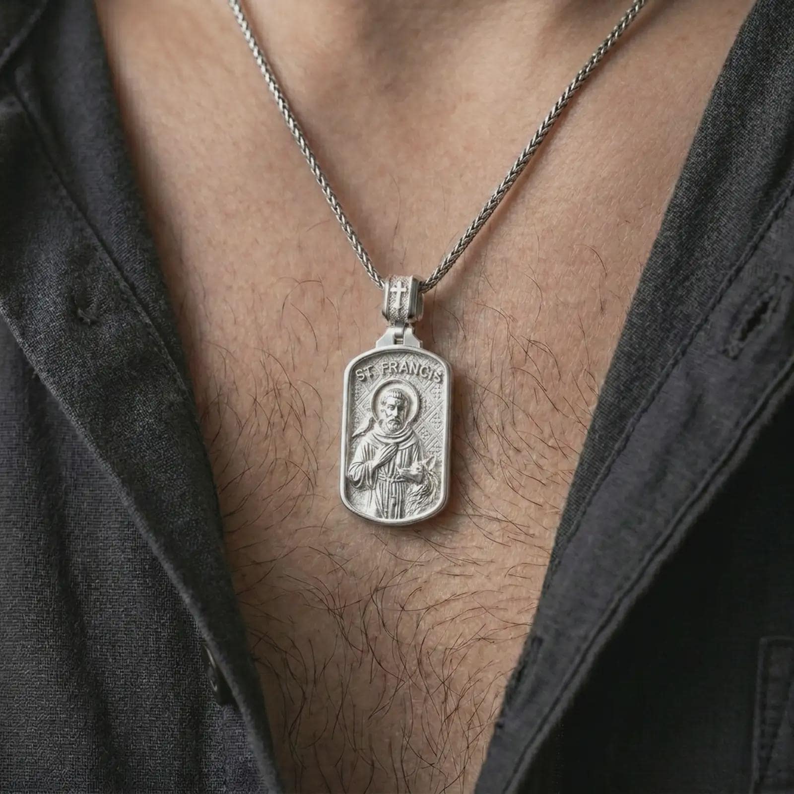 Polished silver Saint Francis pendant necklace worn on the chest, masculine lifestyle shot highlighting the saint relief, bird, wolf detail, and bright silver finish.