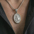 Load image into Gallery viewer, Polished silver Saint Paul pendant necklace worn on the chest, masculine lifestyle shot highlighting the apostle relief, sword, book detail, and bright silver finish.
