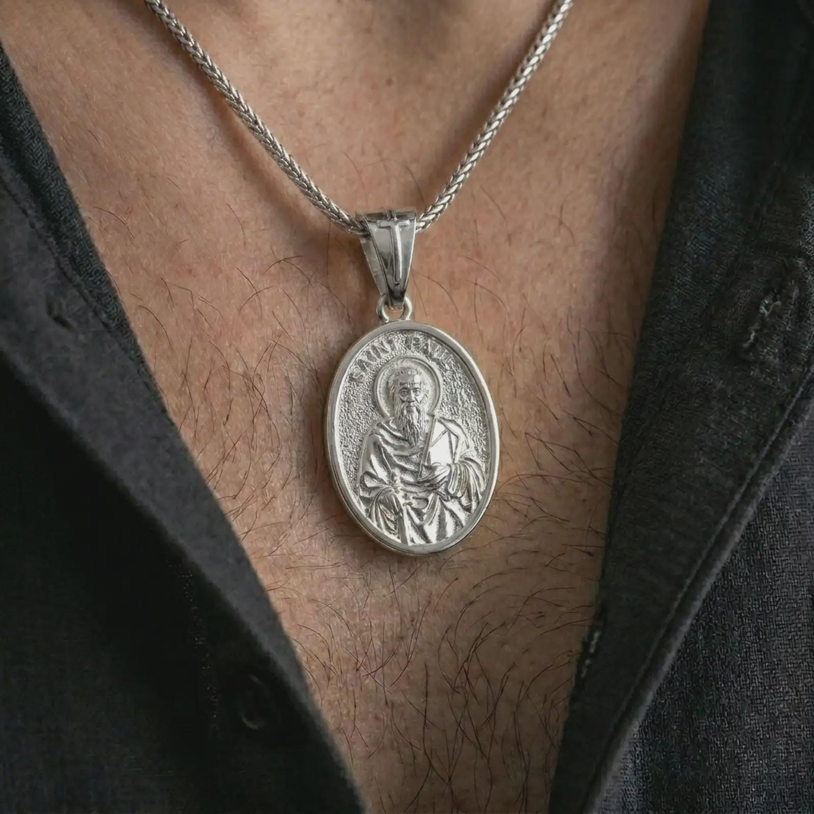 Polished silver Saint Paul pendant necklace worn on the chest, masculine lifestyle shot highlighting the apostle relief, sword, book detail, and bright silver finish.