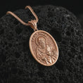 Load image into Gallery viewer, Rose gold plated Saint Paul pendant necklace on textured volcanic rock, detailed macro product shot with soft warm reflections and devotional Saint Paul design.
