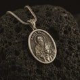 Load image into Gallery viewer, Bronze Saint Paul pendant necklace on textured volcanic rock, close-up studio shot highlighting the apostle relief, sword, book detail, and antique silver contrast.
