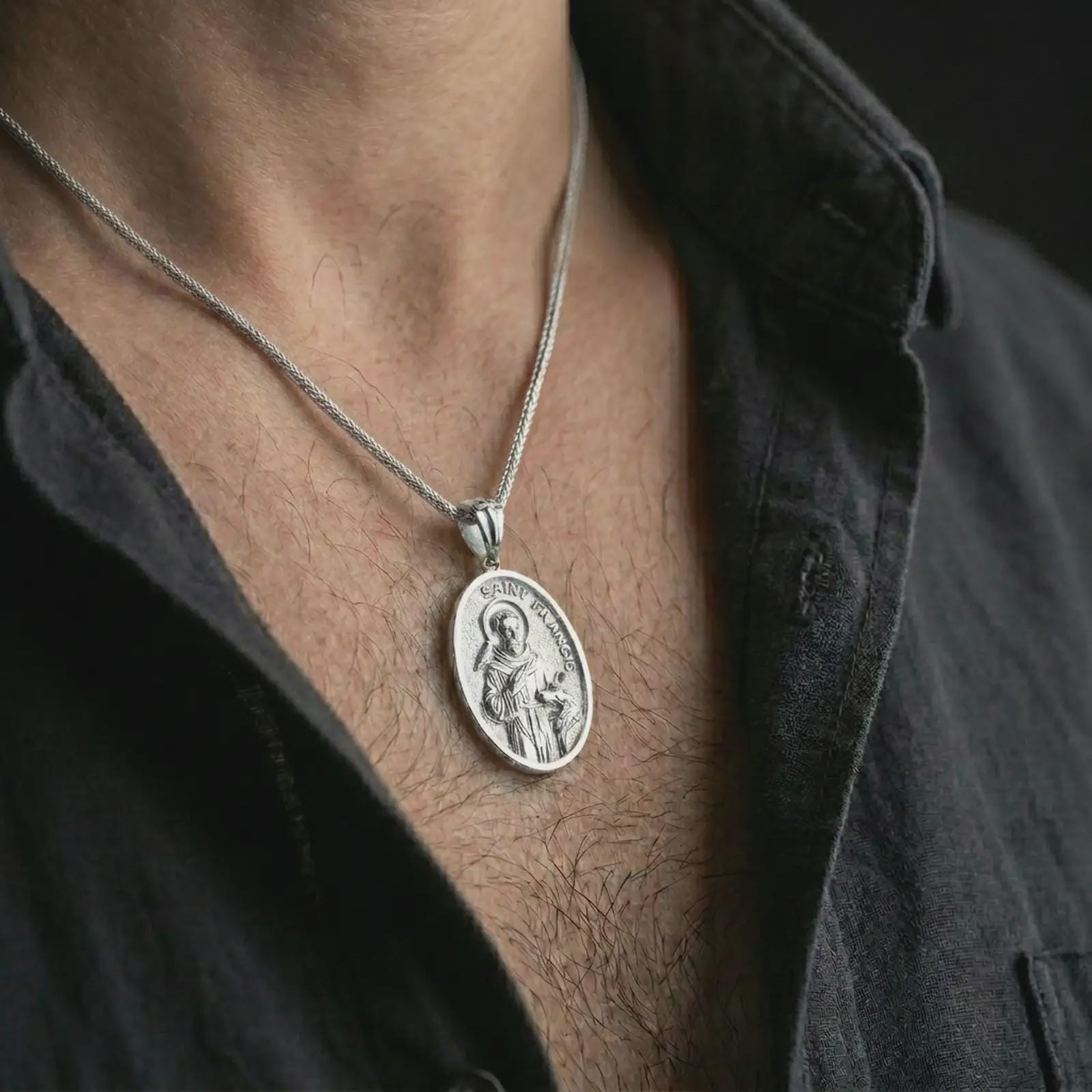 Polished silver Saint Francis pendant necklace worn on the chest, masculine lifestyle shot highlighting the saint relief, bird, wolf detail, and bright silver finish.