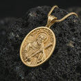 Load image into Gallery viewer, Gold plated Saint Andrew pendant necklace on textured volcanic rock, premium close-up studio composition emphasizing the apostle figure, cross, and sacred book symbolism.
