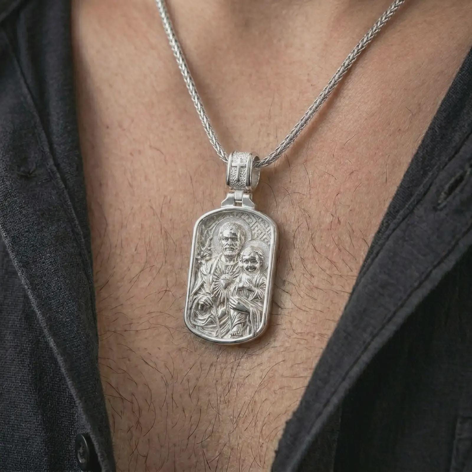 Polished silver Saint Joseph and Jesus pendant necklace worn on the chest, masculine lifestyle shot highlighting the father and child relief, lily detail, and bright silver finish.