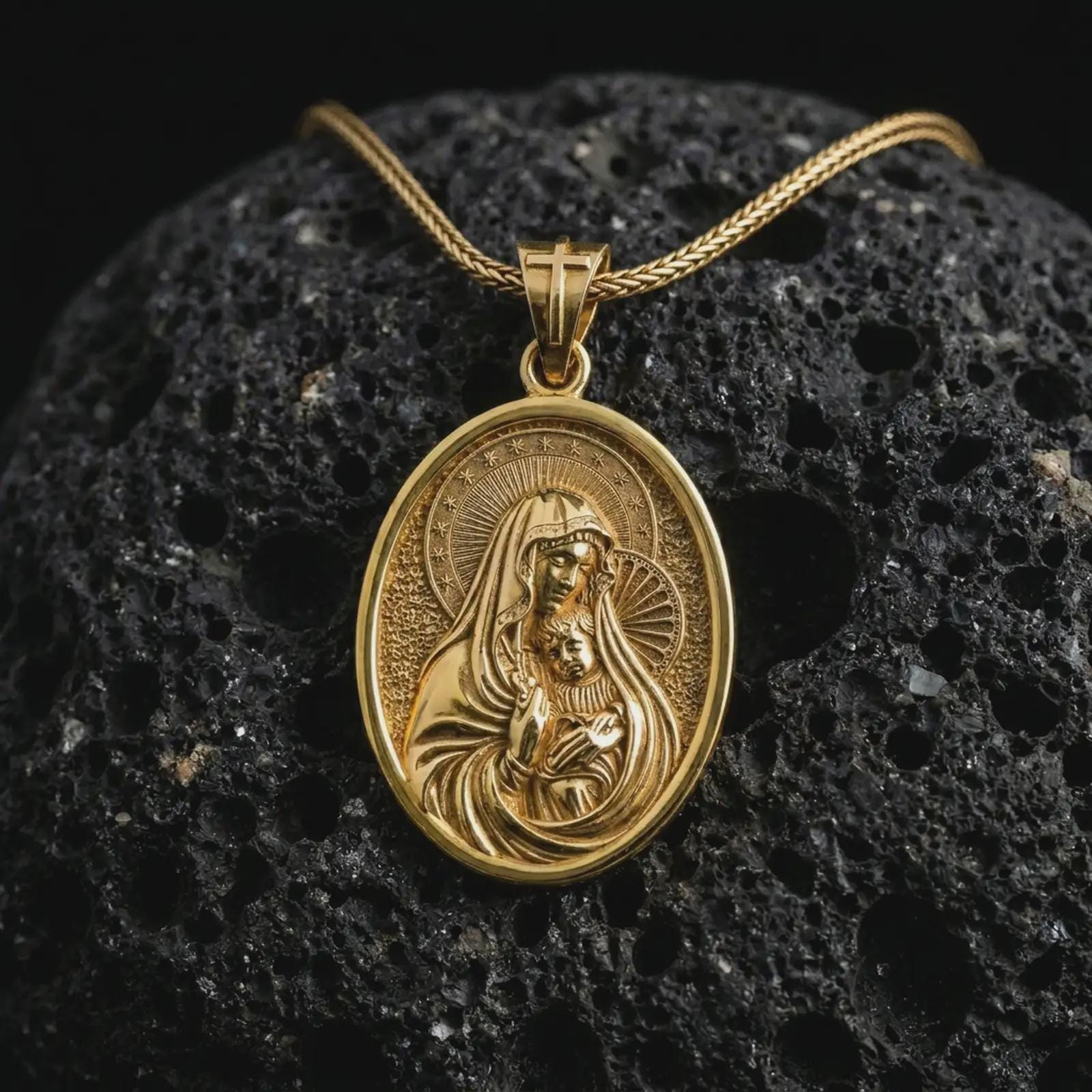 Gold plated Virgin Mary and baby Jesus pendant necklace on textured volcanic rock, premium close-up studio composition emphasizing the Madonna and child design with sacred halo details.