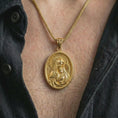 Load image into Gallery viewer, Gold plated Virgin Mary and baby Jesus pendant necklace worn on the chest, premium lifestyle jewelry photo with the sacred mother and child medal centered on a spiga chain.
