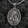 Load image into Gallery viewer, Oxidized Virgin Mary and baby Jesus pendant necklace on textured volcanic rock, close-up studio shot highlighting the mother and child relief, halo, star border, and antique silver contrast.
