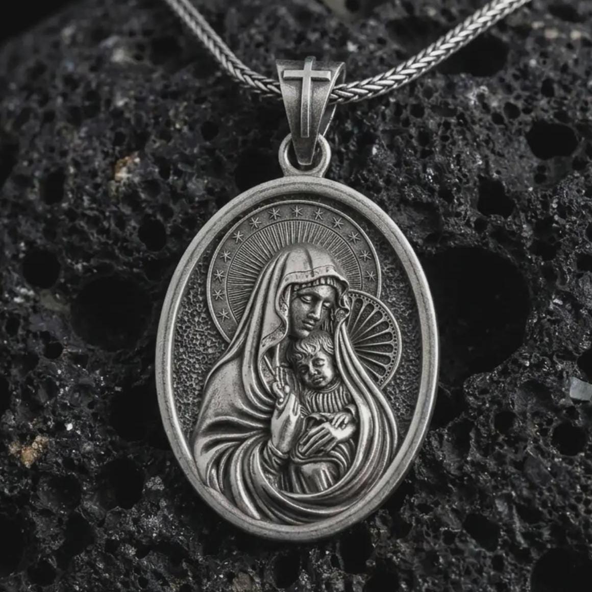 Oxidized Virgin Mary and baby Jesus pendant necklace on textured volcanic rock, close-up studio shot highlighting the mother and child relief, halo, star border, and antique silver contrast.