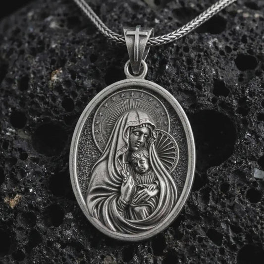 Oxidized Virgin Mary and baby Jesus pendant necklace on textured volcanic rock, close-up studio shot highlighting the mother and child relief, halo, star border, and antique silver contrast.