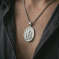 Load image into Gallery viewer, Polished silver Saint Anthony of Padua pendant necklace worn on the chest, masculine lifestyle shot highlighting the saint and child relief, lily detail, and bright silver finish.
