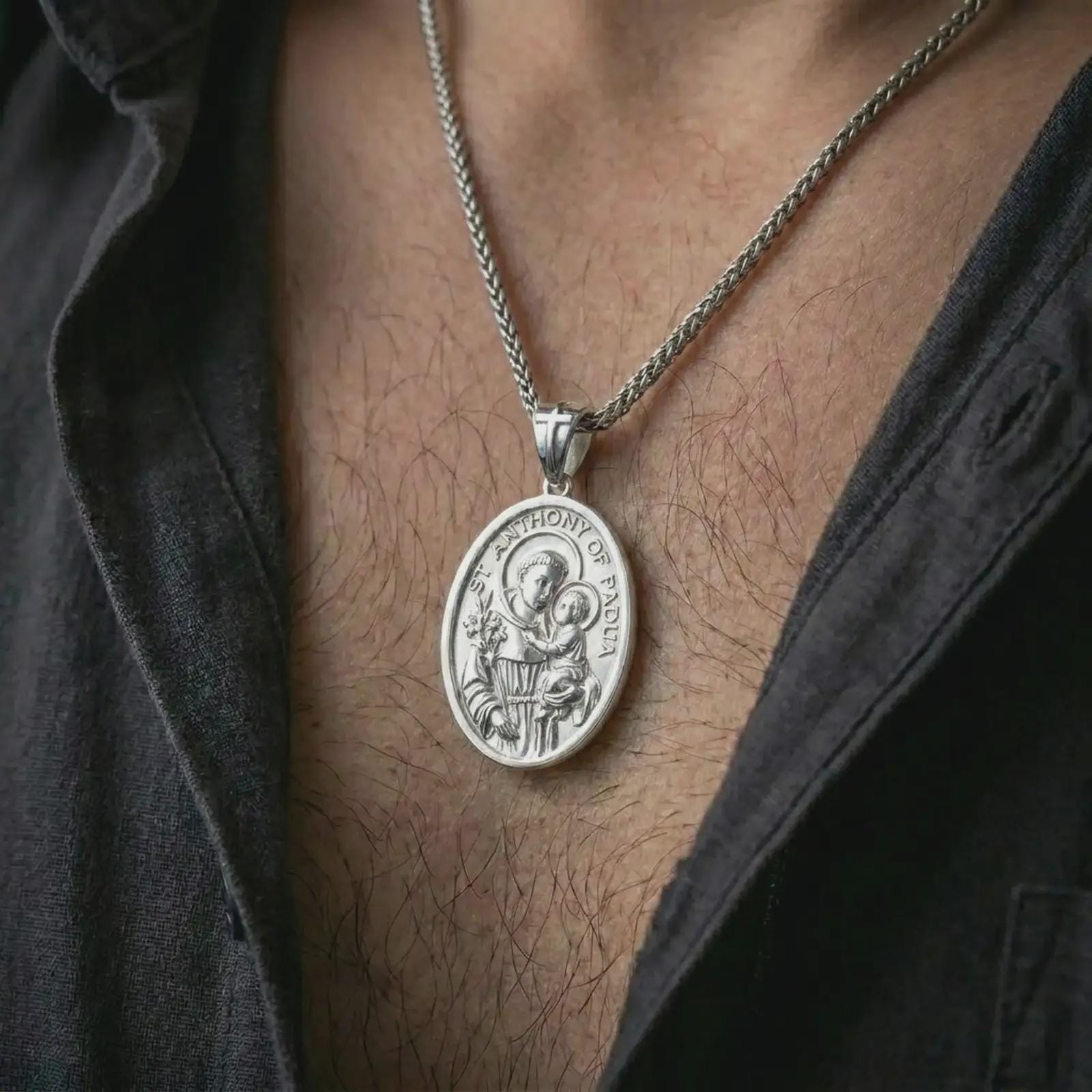 Polished silver Saint Anthony of Padua pendant necklace worn on the chest, masculine lifestyle shot highlighting the saint and child relief, lily detail, and bright silver finish.