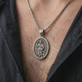 Load image into Gallery viewer, Oxidized Saint Roch pendant necklace worn on the chest, close-up lifestyle jewelry photo showing the Catholic medallion on a spiga chain with dark clothing.
