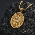 Load image into Gallery viewer, Gold plated Saint Roch pendant necklace on textured volcanic rock, premium close-up studio composition emphasizing the pilgrim saint figure, staff, and faithful dog symbolism.

