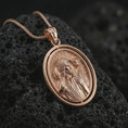 Load image into Gallery viewer, Rose gold plated spinning Good Shepherd pendant necklace on textured volcanic rock, detailed macro product shot with soft warm reflections and sacred shepherd symbolism.

