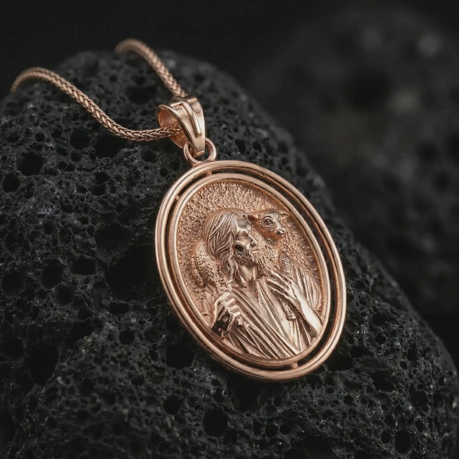 Rose gold plated spinning Good Shepherd pendant necklace on textured volcanic rock, detailed macro product shot with soft warm reflections and sacred shepherd symbolism.