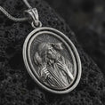 Load image into Gallery viewer, Oxidized spinning Good Shepherd pendant necklace on textured volcanic rock, close-up studio shot highlighting the Jesus and lamb relief with antique silver contrast.
