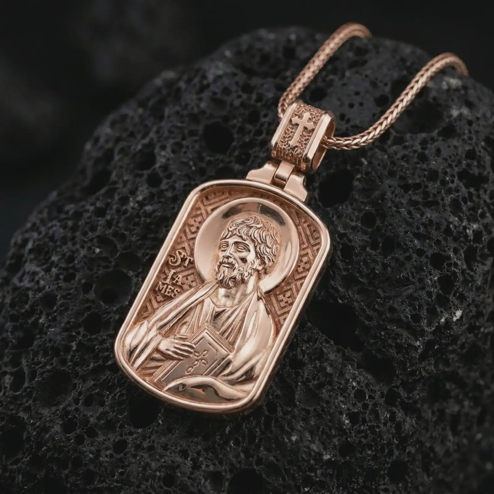 Rose gold plated Saint James the Apostle pendant necklace on textured volcanic rock, detailed macro product shot with soft warm reflections and devotional Saint James design.