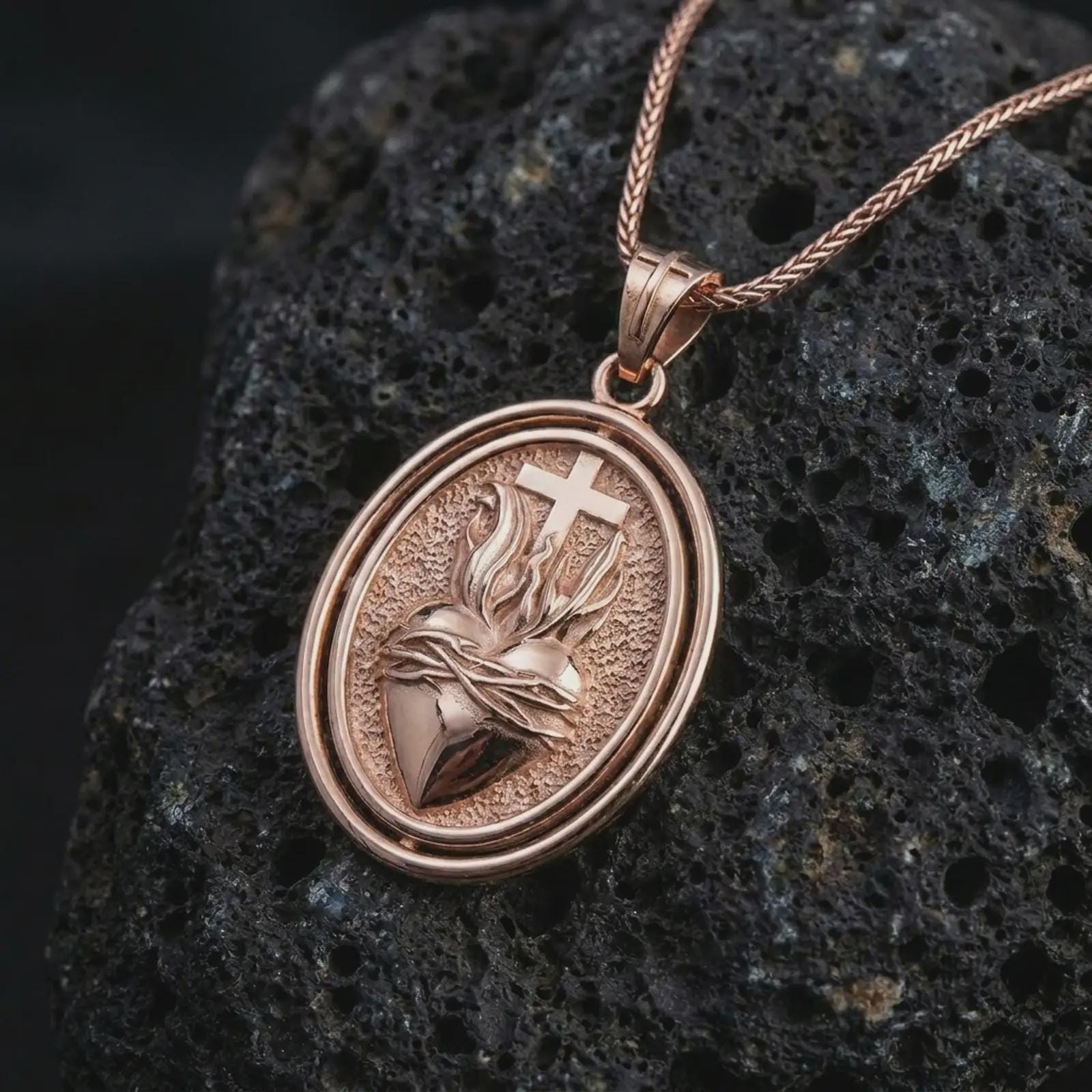 Rose gold plated Sacred Heart pendant necklace on textured volcanic rock, detailed macro product shot with soft warm reflections and devotional heart design.