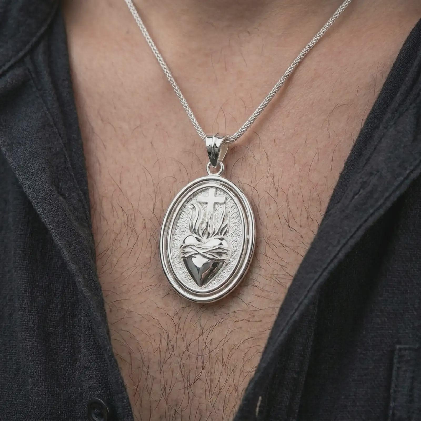 Polished silver Sacred Heart pendant necklace worn on the chest, masculine lifestyle shot highlighting the flaming heart relief, cross detail, and bright silver finish.