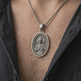 Load image into Gallery viewer, Oxidized Saint Jude pendant necklace worn on the chest, close-up lifestyle jewelry photo showing the Catholic medallion on a spiga chain with dark clothing.
