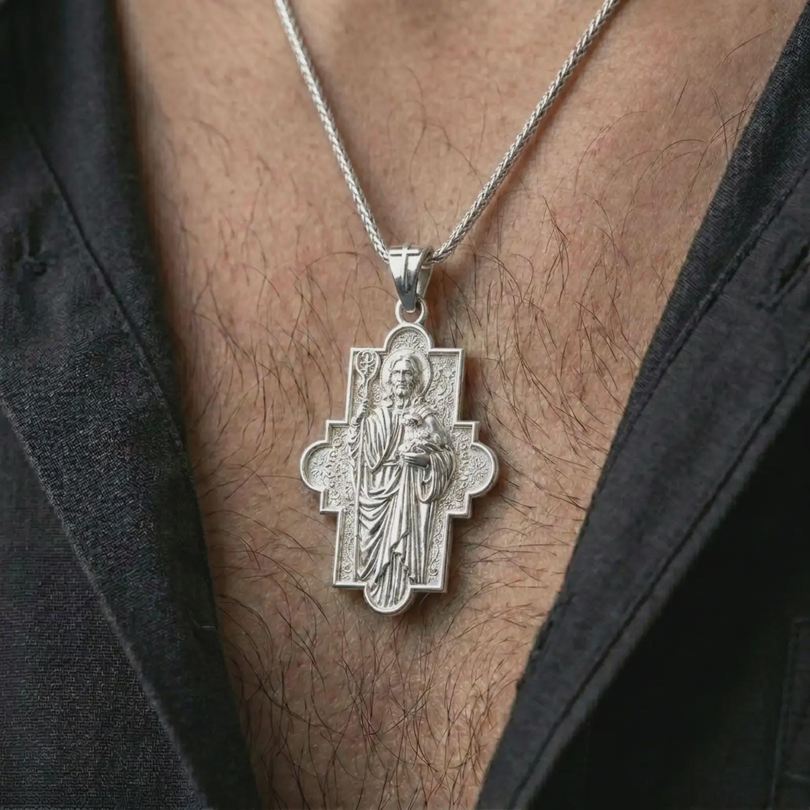 Polished silver Good Shepherd cross pendant necklace worn on the chest, masculine lifestyle shot highlighting the Jesus relief, lamb detail, ornate cross frame, and bright silver finish.